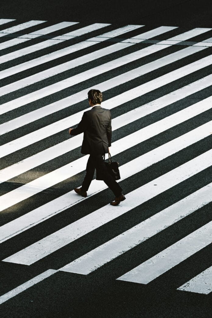 man-in-black-formal-suit-jacket-and-pants-carrying-black-bag-while-walking-on-pedestrian-lane-during-daytime-stockpack-unsplash origini street photography
