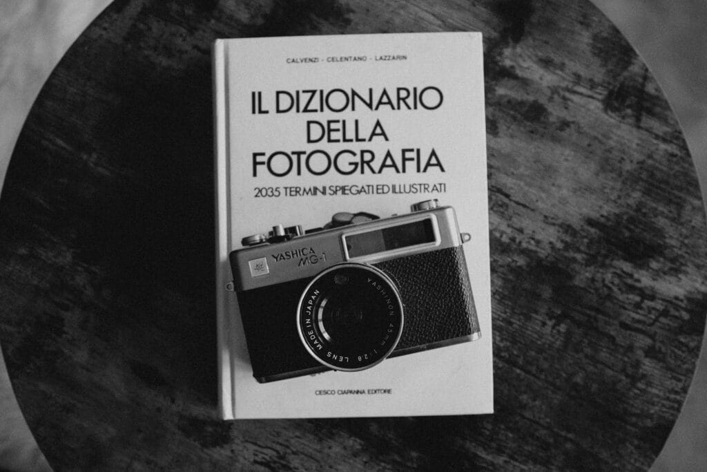 Imparare a fotografare è relativamente semplice. Imparare a vedere è un'altra cosa: richiede tempo, letture, frequentazione dei maestri e soprattutto la capacità di interrogare le immagini con la stessa serietà con cui un critico letterario interroga un testo. Dai sessanta libri fondamentali della cultura fotografica alle analisi ravvicinate degli scatti che hanno cambiato la storia — il momento decisivo di Cartier-Bresson alla Gare Saint-Lazare, il taglio perfetto del Bacio di Doisneau, l'Uomo che cade di Richard Drew, la copertina di Abbey Road — questa guida alla formazione fotografica profonda vuole costruire lo sguardo critico che separa il fotografo che scatta dal fotografo che pensa.Costruire una biblioteca fotografica: dai sessanta classici ai maestri per genere
La prima domanda che ogni fotografo serio si pone, prima o poi, è questa: cosa leggere? La risposta è più complicata di quanto sembri, perché la letteratura fotografica è vastissima, diseguale nella qualità e spesso scritta in una lingua, l'inglese, che non è quella di tutti. Esistono manuali tecnici, monografie d'autore, testi di storia e teoria, raccolte di portfolio, diari di lavoro, interviste. Esistono libri che insegnano la composizione e libri che analizzano il significato politico delle immagini. Esistono cataloghi di mostre che sono capolavori editoriali e testi accademici di quasi illeggibile densità. Navigare in questo oceano senza una bussola è difficile, e la conseguenza più frequente è che molti fotografi rinunciano alla lettura sistematica e si limitano a sfogliare Instagram, che è l'equivalente fotografico di nutrirsi solo di fast food. La formazione fotografica seria richiede invece una dieta più varia e più sostanziosa, costruita con pazienza e con una logica di progressione che va dal generale al particolare, dalla storia alla teoria, dall'analisi delle immagini altrui alla comprensione del proprio modo di guardare.
Il punto di partenza ideale per chiunque voglia costruire una biblioteca fotografica degna di questo nome è la selezione dei sessanta libri di fotografia che ogni appassionato dovrebbe conoscere e leggere. Una lista di sessanta titoli potrebbe sembrare eccessiva per chi si avvicina alla fotografia come hobby, ma in realtà rappresenta appena la superficie di una letteratura enorme: sono i sessanta libri che non si possono non avere letto se si vuole parlare di fotografia con qualche competenza. Tra questi ci sono testi di storia come quella di Beaumont Newhall, la prima grande sintesi storica della fotografia, e quella di Naomi Rosenblum, più ampia e aggiornata. Ci sono i classici della teoria visiva come Camera Lucida di Roland Barthes, che in poche pagine dense ha cambiato il modo in cui si pensa alla fotografia in relazione alla morte e alla memoria, e On Photography di Susan Sontag, che rimane a distanza di decenni il saggio critico sulla fotografia più letto e più discusso al mondo. Ci sono le monografie degli autori imprescindibili — Cartier-Bresson, Arbus, Frank, Winogrand, Salgado — e i portfolios che hanno definito i generi fotografici principali. Leggere questi sessanta libri nell'arco di qualche anno non è un esercizio accademico: è il modo più efficace per acquisire quel background culturale che permette di vedere le proprie fotografie in relazione a una tradizione, e di capire dove ci si colloca nel grande fiume della storia dell'immagine fotografica.
Ma i libri non bastano senza la conoscenza diretta dei maestri della fotografia, quei fotografi che hanno definito i linguaggi visivi che ancora oggi usiamo, spesso senza saperlo. Conoscere i maestri non significa ammirare le loro fotografie in modo generico: significa studiare le loro scelte compositive, capire i loro sistemi di lavoro, leggere le loro dichiarazioni di poetica, confrontare le serie complete piuttosto che le singole immagini famose. Un maestro come Dorothea Lange non si capisce guardando solo la Madre Migrante del 1936 — che è l'immagine per cui è nota al grande pubblico — ma studiando l'intero corpus del suo lavoro per la Farm Security Administration e i suoi scritti sul rapporto tra documentazione sociale e arte fotografica. Un maestro come Garry Winogrand non si capisce guardando le sue fotografie più citate, ma leggendo le sue interviste dove spiega che fotografava non per documentare il mondo ma per vedere come il mondo appariva nell'atto di essere fotografato: una distinzione sottile ma fondamentale per capire la sua estetica del caso controllato. Approfondire i maestri della fotografia significa imparare che dietro ogni grande immagine c'è una visione filosofica del rapporto tra chi guarda, chi è guardato e lo strumento che media questo sguardo.
Per chi preferisce organizzare lo studio per genere fotografico piuttosto che per autore, la guida ai maestri della fotografia per genere fotografico offre un percorso alternativo ma complementare. Ogni genere — ritratto, paesaggio, street photography, documentario, moda, architettura, fotografia scientifica — ha i propri maestri di riferimento, i propri canoni estetici, le proprie tradizioni tecniche e le proprie questioni etiche specifiche. Studiare i maestri del ritratto significa confrontarsi con domande che non si pongono al paesaggista: il rapporto di potere tra fotografo e soggetto, il consenso all'immagine, la responsabilità della rappresentazione di persone reali in contesti privati o pubblici. Studiare i maestri del documentario significa confrontarsi con la questione della veridicità dell'immagine fotografica e con il confine sempre più labile tra documentazione e costruzione. Organizzare la propria formazione fotografica per generi permette di approfondire le questioni specifiche che ciascun tipo di fotografia pone, senza disperdere le energie in una genericità che non porta da nessuna parte. Il consiglio è di scegliere il genere che si pratica, studiarlo a fondo attraverso i suoi maestri, e poi allargarsi ai generi adiacenti con la consapevolezza di chi sa già dove sta andando.
La formazione fotografica non si consuma solo nelle biblioteche e nei musei: passa anche attraverso il confronto diretto con chi ha più esperienza. Il format dell'esperto di fotografia che risponde offre esattamente questo: la possibilità di sottoporre domande specifiche a fotografi esperti e di ricevere risposte che tengono conto del contesto e della situazione concreta di chi chiede. Questo tipo di apprendimento dialogico, che la scuola tradizionale tende a marginalizzare a favore della lezione frontale, è in realtà quello più efficace per la fotografia: i problemi reali che un fotografo incontra sul campo raramente sono quelli descritti nei manuali, e la capacità di adattare i principi generali alle situazioni specifiche è una competenza che si acquisisce attraverso la pratica e il confronto, non attraverso la sola lettura. La storia della Royal Photographic Society, fondata a Londra nel 1853 e tuttora una delle istituzioni fotografiche più autorevoli al mondo, è la storia di un'organizzazione che ha sempre messo al centro proprio questo tipo di apprendimento comunitario e dialettico: l'incontro tra fotografi di diversa esperienza, la discussione delle immagini, la critica costruttiva come strumento di crescita collettiva. La Royal Photographic Society fu la prima istituzione a istituire premi e riconoscimenti fotografici su base qualitativa, contribuendo a definire i canoni estetici che ancora oggi, in modo più o meno consapevole, influenzano il giudizio sulla fotografia di qualità.
Leggere i maestri: da Ansel Adams ad August Sander, dalla composizione alla politica dell'immagine
C'è un modo superficiale di studiare i grandi fotografi e un modo profondo. Il modo superficiale è guardare le loro immagini più note, leggere la biografia in due paragrafi e passare avanti. Il modo profondo è chiedersi cosa c'è dentro quelle immagini, quali scelte le hanno prodotte, cosa raccontano del loro tempo e del loro autore, cosa nascondono sotto la superficie visibile. La analisi fotografica profonda non è un esercizio riservato ai critici accademici: è una competenza che ogni fotografo serio dovrebbe coltivare, perché capire perché una fotografia funziona è il modo più efficace per capire come farne funzionare una propria. I due maestri che prendiamo in esame in questo capitolo — Ansel Adams e August Sander — sono apparentemente distantissimi per soggetto, estetica e funzione sociale della loro fotografia, eppure condividono una caratteristica fondamentale: ogni loro immagine è il risultato di un sistema di pensiero preciso e coerente, applicato con ostinazione per decenni.
Ansel Adams è il fotografo di paesaggio più famoso della storia, ma ridurlo a questo sarebbe un errore di prospettiva. Adams era soprattutto un teorico della composizione fotografica, uno studioso del rapporto tra luce e forma, un costruttore di sistemi. Il suo Sistema Zonale, che divide la scala tonale in undici zone dal nero assoluto al bianco puro e che permette al fotografo di controllare con precisione matematica l'esposizione e lo sviluppo per ottenere il risultato desiderato, è ancora oggi il sistema di riferimento per chiunque lavori con la pellicola in bianco e nero. Ma al di là della tecnica, ciò che rende Adams un maestro da studiare è la sua capacità di trasformare le regole compositive in strumenti di visione: le regole compositive di Ansel Adams applicate alla fotografia di paesaggio non sono prescrizioni rigide ma principi di organizzazione dello spazio visivo che possono essere applicati, con gli opportuni adattamenti, anche alla fotografia digitale e persino alla fotografia con lo smartphone. La lezione di Adams è che la composizione non è un ornamento dell'immagine ma la sua struttura portante: cambiare la composizione di una fotografia significa cambiare il suo significato, non solo la sua estetica. Chi studia Adams con attenzione impara a guardare il mondo in termini di masse tonali, di linee di forza e di relazioni spaziali prima ancora di premere il pulsante di scatto, e questo cambia irreversibilmente il modo in cui si fotografa.
La distanza tra Adams e August Sander non potrebbe essere più grande: il primo fotografava montagne e deserti in un'America che stava costruendo la propria mitologia naturalistica, il secondo fotografava persone in una Germania che stava costruendo la propria tragedia politica. Eppure entrambi condividevano un rigore metodologico assoluto e una visione del progetto fotografico come opera di lungo respiro, non come raccolta di immagini occasionali. Il progetto di Sander, Uomini del Ventesimo Secolo, era un atlante fotografico della società tedesca del primo Novecento: ritratti di persone di ogni classe sociale, ogni professione e ogni origine, realizzati con una tecnica uniforme e un approccio sistematico che mirava a costruire un inventario visivo completo dell'umanità tedesca del suo tempo. Ma leggere i ritratti di Sander come semplice documentazione sociologica significa perderne la dimensione più interessante: quella dei messaggi politici nascosti nelle fotografie di August Sander. Sander fotografava con uno sguardo apparentemente neutro, che trattava il contadino e il banchiere con la stessa distanza formale, la stessa luce, lo stesso formato. Ma questa neutralità apparente era in realtà una scelta politica potente: in un'epoca in cui la fisiognomica pseudoscientifica pretendeva di leggere il carattere, l'intelligenza e la razza dal volto delle persone, Sander dimostrava attraverso le sue immagini che ogni classificazione gerarchica era arbitraria e che l'umanità era irriducibile a tipologie. Non è un caso che i nazisti, dopo l'ascesa al potere nel 1933, confiscassero e distruggessero le lastre di Sander: avevano capito meglio di molti critici moderni la natura eversiva di quel progetto apparentemente neutro.
Lo studio dei maestri attraverso la loro opera richiede anche la capacità di contestualizzare storicamente e socialmente il loro lavoro. La analisi fotografica di Sander non si può separare dalla storia della Repubblica di Weimar e dall'ascesa del nazismo, così come la cultura visiva di Adams non si può separare dal movimento ambientalista americano e dal ruolo del Sierra Club nella protezione dei parchi nazionali. Capire in quale contesto un'immagine è stata prodotta non significa ridurla a documento storico: significa aggiungere alla comprensione estetica una comprensione delle forze culturali e politiche che l'hanno resa possibile e necessaria. I grandi fotografi non fotografano nel vuoto: fotografano in risposta al mondo che li circonda, e le loro immagini portano sempre, in modo più o meno esplicito, i segni di questo dialogo con la realtà storica.
Un caso particolare di questo dialogo tra fotografia e potere è quello di Richard Avedon, il cui modo di fare ritratto fotografico era tutto fuorché neutro nonostante l'apparenza di semplicità formale. I ritratti di Avedon — fondo bianco, luce piatta, soggetto molto vicino alla macchina — sembrano eliminare ogni elemento di distrazione per portare all'essenziale il rapporto tra fotografo e soggetto. Ma è esattamente qui che sta la forza e la violenza latente del suo approccio: come analizza in profondità lo specchio deformante del rapporto tra fotografo e soggetto nei ritratti di Avedon, la semplicità formale di Avedon era una trappola per i soggetti, che si trovavano privati di ogni schermo protettivo — l'abbigliamento, l'ambiente, gli oggetti di scena — e costretti a confrontarsi con la macchina fotografica in modo frontale e totale. Il risultato era spesso di una crudezza psicologica che i soggetti stessi non si aspettavano: Avedon fotografava il potere — presidenti, CEO, attori famosi — con la stessa implacabilità con cui fotografava gli anziani del West americano, e in entrambi i casi il risultato era un'immagine che mostrava qualcosa che il soggetto probabilmente avrebbe preferito non mostrare. La questione del potere nel ritratto fotografico — chi ha potere su chi, chi decide come l'altro appare — è una delle più importanti della cultura visiva contemporanea, e Avedon ne è il caso di studio più istruttivo.
Anatomia di un capolavoro: il momento decisivo, il taglio perfetto e la fotografia come evento
Ci sono fotografie che si guardano e si passa avanti. E ci sono fotografie davanti alle quali ci si ferma, si torna indietro, ci si chiede come sia stato possibile. La differenza tra le une e le altre non è quasi mai nella soggettività dello spettatore: è nella struttura dell'immagine, nel modo in cui ogni suo elemento contribuisce a un insieme che funziona con una coerenza quasi impossibile da spiegare razionalmente ma reale e verificabile. L'analisi di queste fotografie — di come sono state realizzate, di cosa le rende indistruttibili nel tempo, di perché continuano a parlare a spettatori di epoche e culture diverse — è uno degli esercizi formativi più efficaci che esistano per chi vuole affinare il proprio sguardo. Non si tratta di scoprire la formula magica della fotografia perfetta, che non esiste, ma di capire quali problemi visivi queste immagini hanno risolto in modo esemplare, e di usare questa comprensione come strumento per affrontare i propri problemi visivi con maggiore consapevolezza.
La fotografia più analizzata, più citata e più imitata di tutta la storia della street photography è probabilmente quella scattata da Henri Cartier-Bresson dietro la Gare Saint-Lazare nel 1932. L'uomo che salta sopra una pozzanghera, il riflesso nell'acqua, il poster sullo sfondo che ripete la figura saltante, la perfezione geometrica dei cerchi concentrici nell'acqua e del profilo circolare che si rispecchia: tutto in questa fotografia funziona con una precisione che sembra impossibile per uno scatto rubato, non costruito. Cartier-Bresson teorizzò il concetto di momento decisivo — l'istante in cui tutti gli elementi visivi si allineano in modo perfetto — e questa fotografia è la sua dimostrazione più completa. Ma studiare la Gare Saint-Lazare significa anche capire ciò che l'analisi superficiale tende a dimenticare: Cartier-Bresson non aspettava passivamente che il momento decisivo accadesse. Frequentava luoghi, tornava più volte, studiava le geometrie preesistenti dello spazio e aspettava che un soggetto vi si inserisse nel modo giusto. Il momento decisivo era il risultato di una preparazione metodica, non di una fortuna casuale. Questa distinzione è fondamentale per la formazione fotografica: il caso nella fotografia esiste, ma i fotografi che lo sfruttano al meglio sono quelli che si sono preparati a riconoscerlo quando arriva.
Altrettanto illuminante, per ragioni diverse, è lo studio del Bacio di Robert Doisneau e in particolare della questione che raramente viene affrontata: perché il taglio originale è perfetto e le varianti no. L'analisi di perché un centimetro può cambiare la storia: il taglio originale del Bacio di Doisneau e perché è perfetto porta direttamente al cuore del problema compositivo: la differenza tra un'immagine che funziona e una che quasi funziona è spesso di dimensioni millimetriche, di rapporti proporzionali che all'occhio conscio sembrano equivalenti ma che all'occhio inconscio producono sensazioni radicalmente diverse. Il Bacio di Doisneau — scattato nel 1950 davanti all'Hôtel de Ville di Parigi e diventato una delle immagini più riprodotte del Novecento — ha nel suo taglio originale un equilibrio tra la coppia che si bacia, il passante sullo sfondo e il bordo dell'inquadratura che non è replicabile spostando di qualche centimetro il bordo dell'immagine senza perdere qualcosa di essenziale. Studiare perché questo accade significa sviluppare quella sensibilità ai rapporti proporzionali interni all'immagine che è la componente più difficile da insegnare e più difficile da acquisire della cultura visiva: non si impara leggendo, si impara guardando migliaia di immagini con attenzione critica e confrontando quelle che funzionano con quelle che quasi funzionano.
Non tutte le fotografie iconiche sono nate dalla ricerca estetica. Alcune sono diventate icone malgrado se stesse, perché il momento storico che documentavano era di una tale potenza che qualsiasi immagine avrebbe acquisito un peso insopportabile. L'Uomo che cade del 2001 di Richard Drew appartiene a questa categoria: scattata l'11 settembre 2001 durante il crollo delle Torri Gemelle, ritrae una persona che cade nel vuoto dalla Torre Nord. Questa fotografia pone alla analisi fotografica domande di un tipo completamente diverso rispetto a quelle che pone Cartier-Bresson o Doisneau: non domande di composizione o di momento decisivo, ma domande etiche sulla responsabilità del fotografo che documenta una morte, sul diritto alla privacy del soggetto in un momento di estrema vulnerabilità, sul rapporto tra il dovere di documentare la storia e il rispetto per la dignità umana. L'immagine di Drew fu pubblicata da molti giornali il giorno dopo gli attentati e poi ritirata dalla circolazione sotto la pressione dell'opinione pubblica americana, che la trovava irrespettosa verso le vittime. Il dibattito che ne seguì — sull'etica del fotogiornalismo, sui limiti della rappresentazione della morte, sul ruolo delle immagini nel lutto collettivo — è uno dei più importanti della storia della cultura visiva contemporanea, e non si può affrontare seriamente la fotografia documentaria senza aver riflettuto a fondo su questa immagine e sulle questioni che solleva.
Un'ultima analisi d'autore che merita attenzione in questo contesto è quella relativa alla copertina di Abbey Road dei Beatles, fotografata da Iain Macmillan nel 1969. Si potrebbe pensare che una copertina discografica sia un territorio marginale per una discussione sulla formazione fotografica seria, ma questa fotografia è in realtà uno dei casi di studio più istruttivi sulla semplicità come scelta coraggiosa. Macmillan aveva a disposizione dieci minuti di riprese sulla zebra davanti agli studi di Abbey Road a Londra, sei lastre e un concetto essenziale: i quattro Beatles che camminano in fila. Nessuno sfondo artificiale, nessuna elaborazione, nessun simbolismo esplicito — solo quattro persone che attraversano una strada nel modo più naturale possibile. Eppure la fotografia risultante ha una forza visiva e una capacità di evocare un'epoca che poche immagini della storia del rock hanno raggiunto. La lezione è quella della sottrazione: togliere elementi, semplificare l'inquadratura, eliminare tutto ciò che non è strettamente necessario porta spesso risultati più potenti dell'accumulo di significati e simboli. È una lezione che vale nella fotografia di moda, nel ritratto, nel reportage e in qualsiasi altro genere: la semplicità non è povertà di idee, è chiarezza di visione.
Costruire uno sguardo critico: dalla teoria alla pratica quotidiana della formazione visiva
La formazione fotografica non è un processo con una fine definita. Non esiste il momento in cui si può dire di aver imparato abbastanza, di aver letto abbastanza, di aver guardato abbastanza. È invece un processo continuo, fatto di spirali che tornano sugli stessi autori e sugli stessi temi con occhi sempre diversi: le fotografie di Cartier-Bresson che si guardano a vent'anni sembrano completamente diverse da quelle che si guardano a quaranta, non perché le fotografie siano cambiate, ma perché è cambiata la propria capacità di vederle. Questo è il senso profondo della cultura visiva: non un corpus di conoscenze da accumulare, ma una capacità di sguardo da affinare continuamente attraverso l'esposizione sistematica a immagini di qualità e alla riflessione critica su di esse. La buona notizia è che questa formazione non richiede frequentare un'accademia o vivere in una grande città: richiede metodo, curiosità e la disponibilità a mettere in discussione le proprie certezze ogni volta che un'immagine eccezionale le sfida.
Il metodo più efficace per sviluppare uno sguardo critico è quello che potremmo chiamare della lettura parallela: leggere la teoria e guardare le immagini contemporaneamente, verificando continuamente i concetti teorici sulle immagini concrete e usando le immagini concrete per affinare la comprensione dei concetti teorici. Leggere Barthes senza guardare fotografie è come leggere un manuale di nuoto senza toccare l'acqua: si acquisiscono concetti, ma non si sviluppa la competenza pratica che solo la frequentazione diretta del materiale può dare. Al contrario, guardare fotografie senza leggere teoria è come nuotare senza capire perché si galleggia: si può anche essere bravi, ma senza la comprensione dei principi che sottendono la propria pratica si rimane intrappolati in ciò che già si sa fare, incapaci di crescere in modo sistematico. La formazione fotografica efficace intreccia costantemente questi due livelli, usando la lettura per problematizzare l'esperienza visiva e l'esperienza visiva per dare carne ai concetti astratti della lettura.
Un secondo elemento fondamentale della formazione è la frequentazione delle istituzioni: musei, gallerie, festival fotografici, biblioteche specializzate. La Royal Photographic Society, già citata, è un esempio di istituzione che ha costruito nel tempo un sistema di premi, mostre e pubblicazioni che costituisce un archivio vivente della storia della fotografia britannica e mondiale. Ma simili istituzioni esistono in quasi tutti i paesi: il MoMA di New York con la sua collezione fotografica, il Jeu de Paume di Parigi, la Deutsche Fotothek di Dresda, il Victoria and Albert Museum di Londra, la Fotostiftung Schweiz di Winterthur. Frequentare queste istituzioni — anche solo attraverso i loro archivi digitali online — significa esporre continuamente il proprio sguardo a fotografie di qualità certificata, costruendo gradualmente quella capacità di discriminazione visiva che è alla base di qualsiasi analisi fotografica seria. La differenza tra un fotografo che ha frequentato musei e gallerie per anni e uno che non lo ha fatto non è nella tecnica: è nella ricchezza del repertorio visivo interno, in quella biblioteca mentale di immagini di riferimento che permette di riconoscere la qualità quando la si vede e di capire cosa manca quando non c'è.
Il terzo elemento, forse il più trascurato, è la scrittura. Scrivere di fotografia — anche solo per sé stessi, in un diario di lavoro o in un quaderno di appunti — costringe a chiarire i propri pensieri in modo che il solo guardare non richiede. Quando si prova a spiegare perché una fotografia funziona, ci si rende conto di quanto sia difficile articolare in parole ciò che l'occhio riconosce istintivamente, e questa difficoltà è formativa: obbliga a sviluppare un vocabolario critico, a precisare i concetti, a distinguere le sensazioni soggettive dagli elementi oggettivi dell'immagine. I grandi fotografi che hanno anche scritto — Adams con il suo sistema, Cartier-Bresson con L'istante decisivo, Arbus con le sue lettere — ci hanno lasciato non solo le immagini ma la chiave per leggere le immagini, e questa doppia testimonianza è di un valore formativo inestimabile. Imparare a scrivere di fotografie, anche in modo rudimentale e privato, è uno degli esercizi più efficaci per sviluppare quella coscienza critica del proprio lavoro che separa il fotografo riflessivo da quello puramente istintivo.
La formazione fotografica seria è, in definitiva, un'educazione dello sguardo nel senso più pieno del termine: un processo che non riguarda solo la fotografia ma il modo in cui si guarda il mondo, si interpretano le immagini, si costruisce il significato di ciò che si vede. Chi si forma seriamente come fotografo — attraverso i libri fondamentali, attraverso lo studio dei maestri per genere, attraverso l'analisi ravvicinata delle fotografie iconiche che hanno fatto la storia — acquisisce qualcosa che va ben al di là della capacità tecnica di produrre immagini tecnicamente corrette: acquisisce la capacità di vedere, che è la cosa più rara e più preziosa che un fotografo possa avere, e che nessuna macchina fotografica, nessun obiettivo e nessun software di post-produzione potrà mai sostituire.
Fonti di approfondimento
Per chi voglia costruire una formazione fotografica solida e sistematica, due risorse di riferimento internazionale sono imprescindibili:
MoMA – Photography Collection & Essays: il Museo di Arte Moderna di New York mette a disposizione online non solo la propria collezione fotografica — tra le più importanti al mondo — ma anche saggi critici, interviste ad autori e materiale didattico sulla analisi fotografica e sulla storia della cultura visiva del Novecento. È un punto di partenza gratuito e autorevole per qualsiasi percorso di formazione fotografica seria.
Royal Photographic Society – Learning Resources: la società fotografica più antica del mondo mette a disposizione dei propri soci e, parzialmente, del pubblico generale un vasto archivio di risorse formative sulla tecnica, sulla storia e sulla teoria della fotografia, con particolare attenzione al rapporto tra cultura visiva e pratica fotografica professionale. Le fellowship e le distinzioni della RPS rimangono i riconoscimenti fotografici più autorevoli nel mondo anglosassone.
