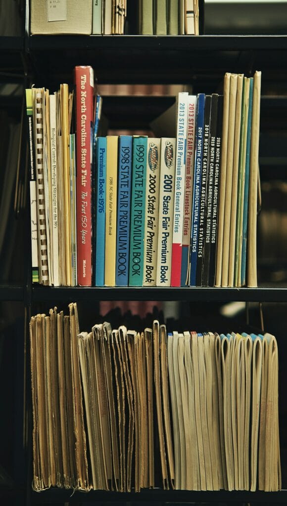 Old documents and books on a black, metal library shelf.